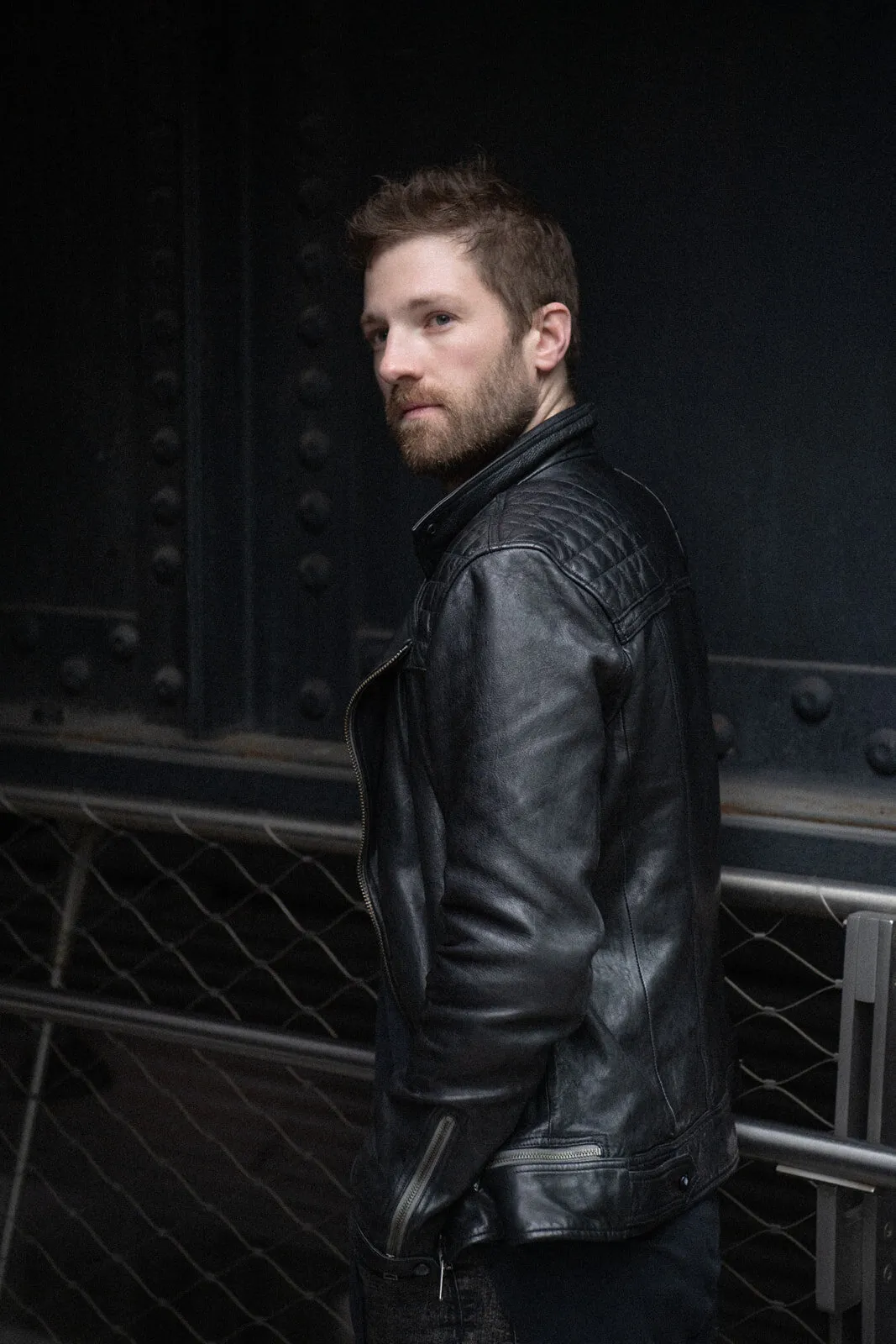 Environmental portrait of a man in a leather jacket against dark steel